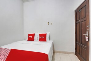Un dormitorio con una cama, dos almohadas rojas, un armario de madera y una puerta con picaporte.