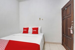 Un dormitorio con una cama, dos almohadas rojas, un armario de madera y una puerta con picaporte.