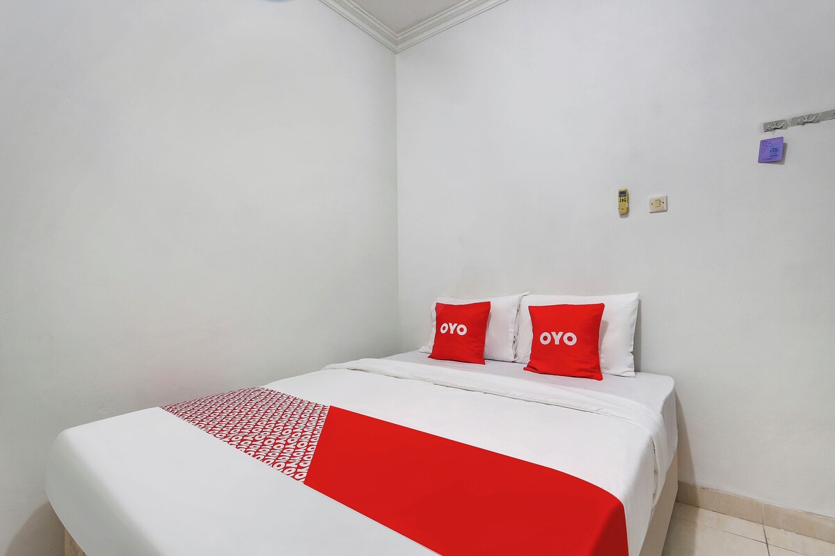 Ein Hotelzimmer mit einem Bett, weißen Wänden und einer rot-weißen Tagesdecke.