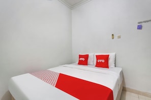 Un lit simple avec une couvre-lit blanche et rouge, deux oreillers rouges ornés du mot « OYO », et un petit objet violet accroché au mur.