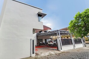Ein modernes Gebäude mit weißer Fassade, einem überdachten Parkbereich und einem Baum rechts.