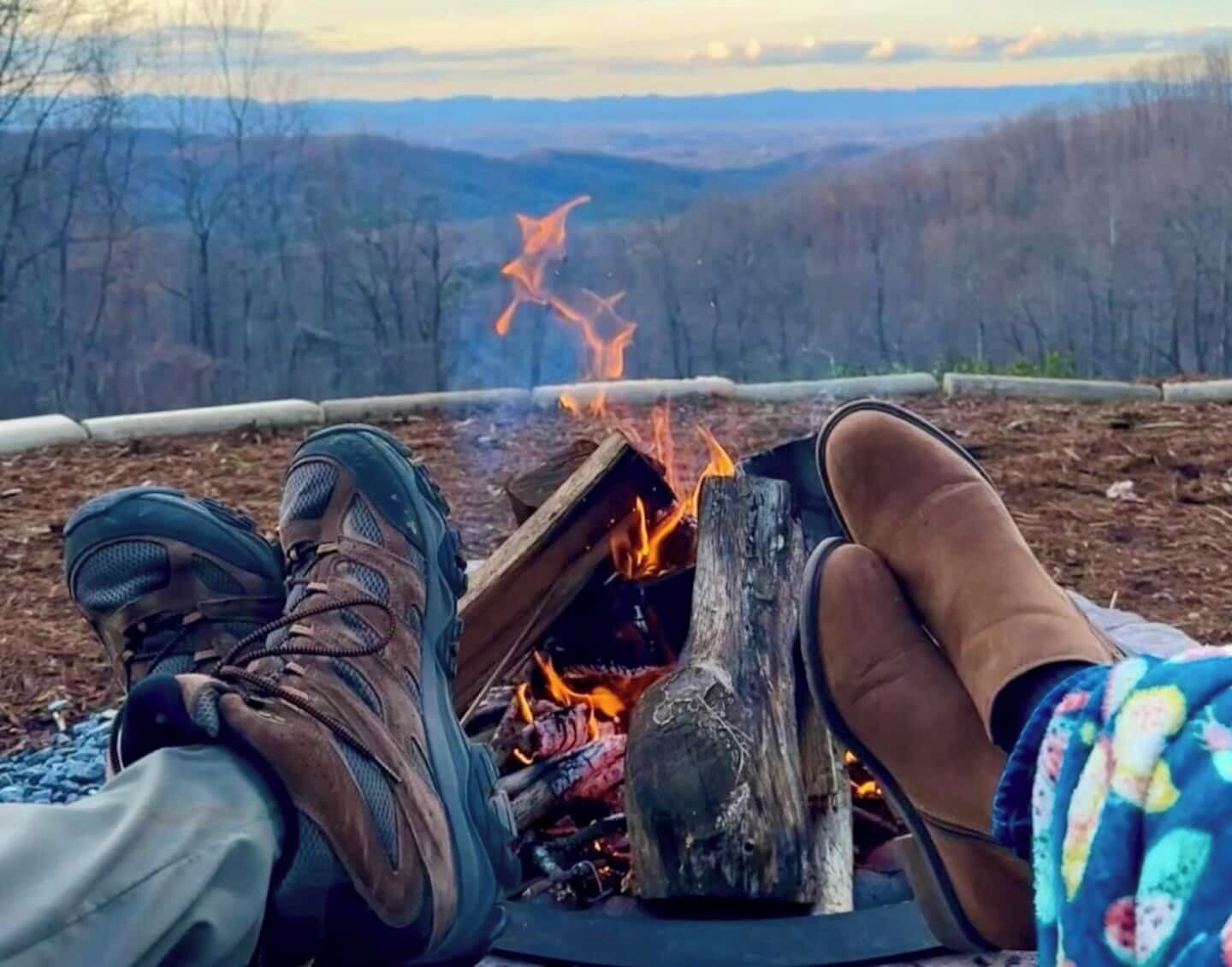 A person relaxing by a campfire with a view of a forested landscape.