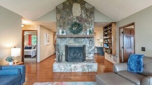 A living room with a stone fireplace, wooden flooring, a blue sofa, a gray sofa, and a bookshelf. - Fall Colors | Prayer Mountain View Cabin | Fabulous Views from Fire Pit | Ping Pong (Moravian Falls)