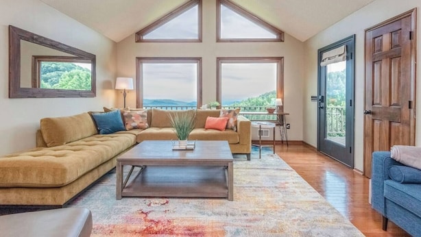 A spacious living room with a high ceiling, large windows, a sofa, a coffee table, and a view of the outdoors.