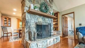 A stone fireplace with a mantel shelf, wooden dining table, and chairs in a living room with hardwood flooring.