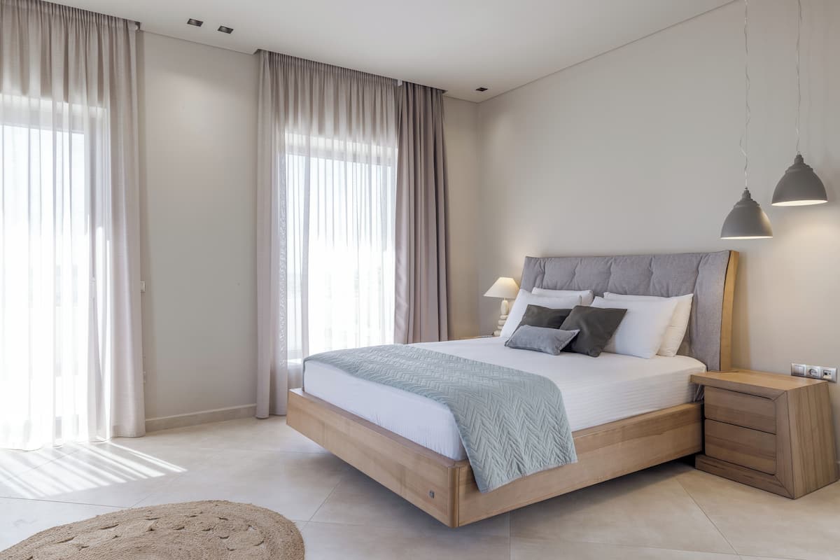 A modern bedroom with a large bed, wooden nightstands, a bedside lamp, and sheer curtains.