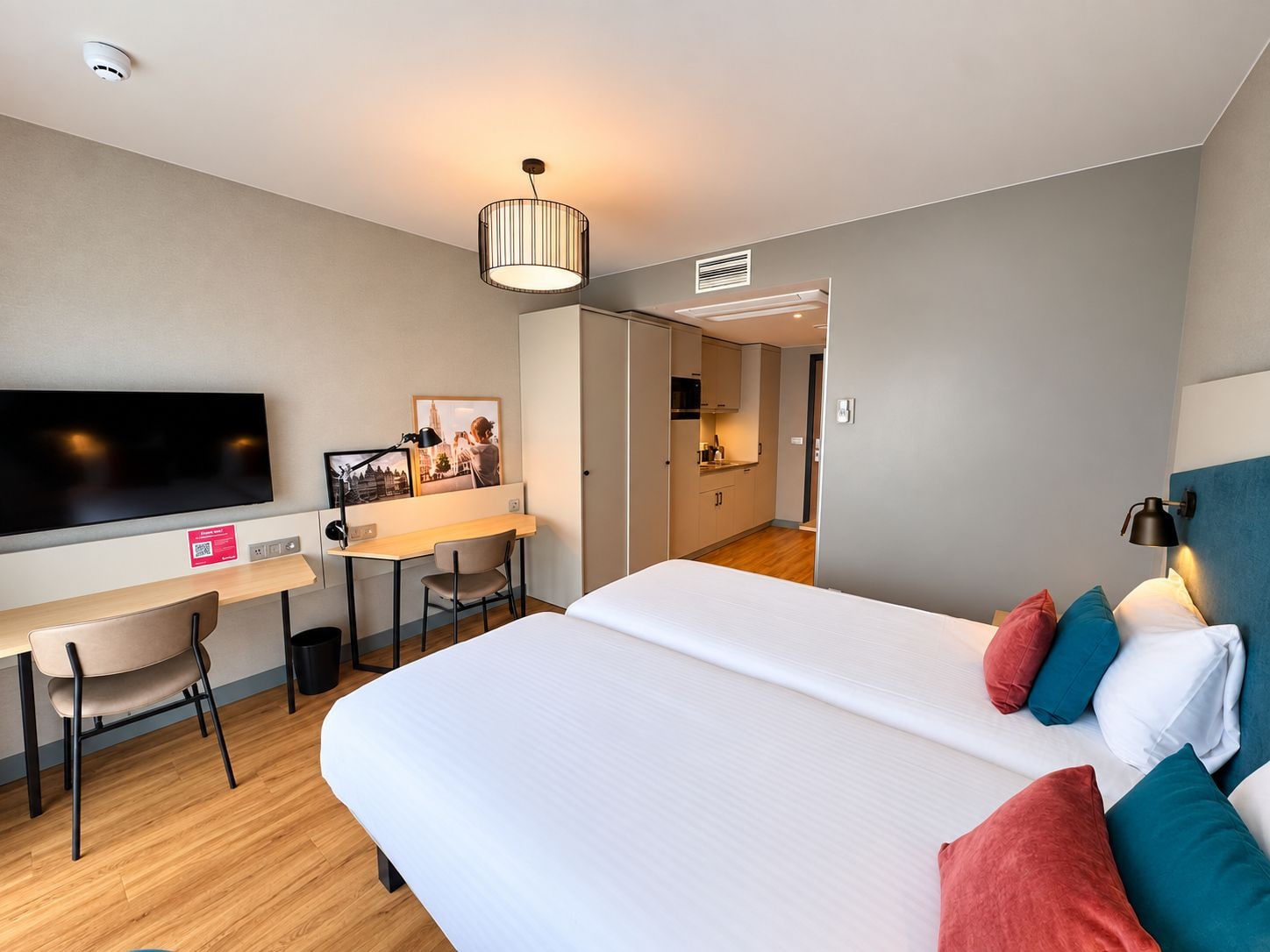 A hotel room with a bed, a desk, a chair, a television, and a kitchenette.