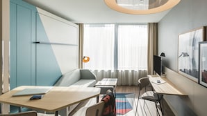 A modern hotel room with a sofa, a desk, a laptop, a smartphone, and a TV. - Adagio Antwerp City Center (Antwerp)