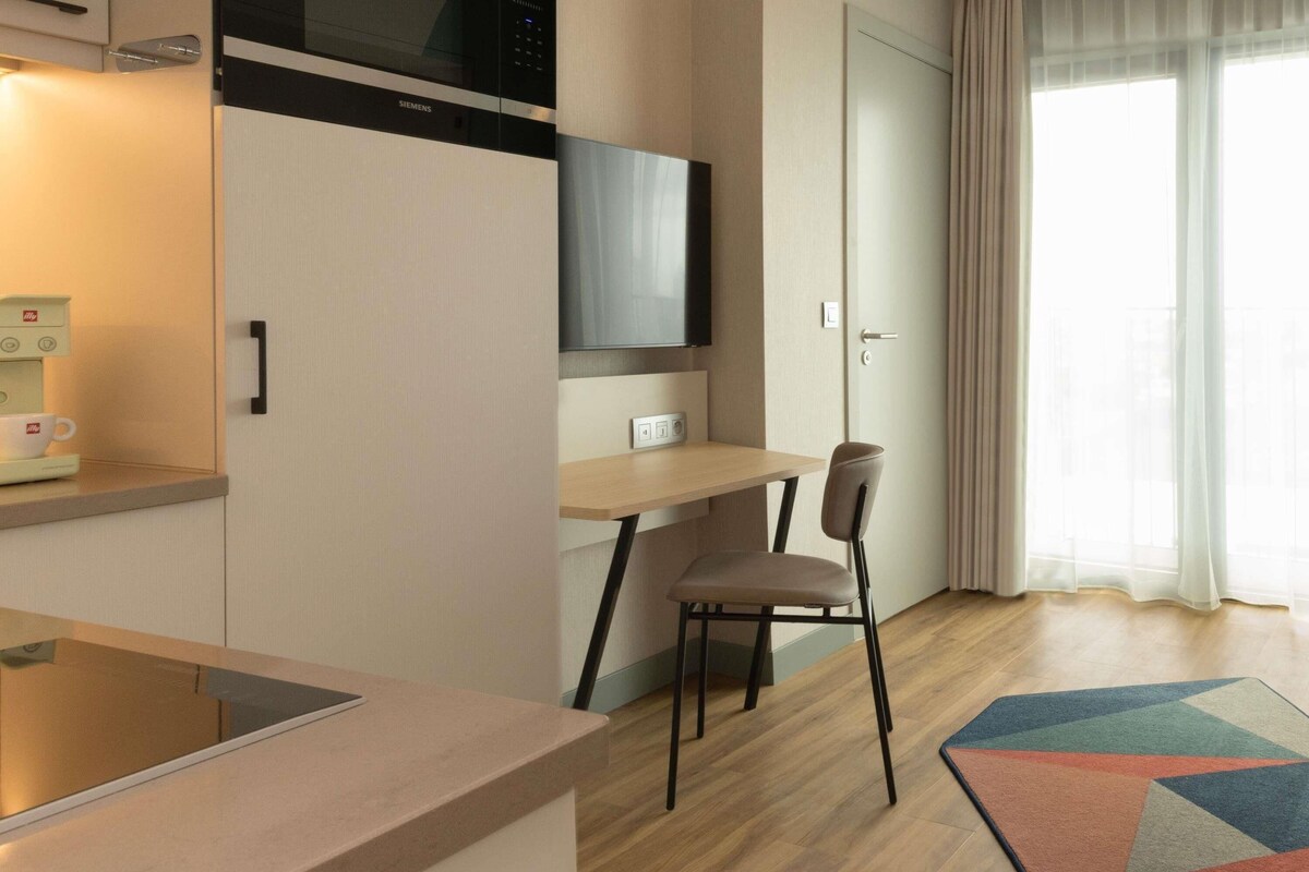 A modern kitchen with a built-in microwave, a coffee machine, and a dining area with a chair and table.