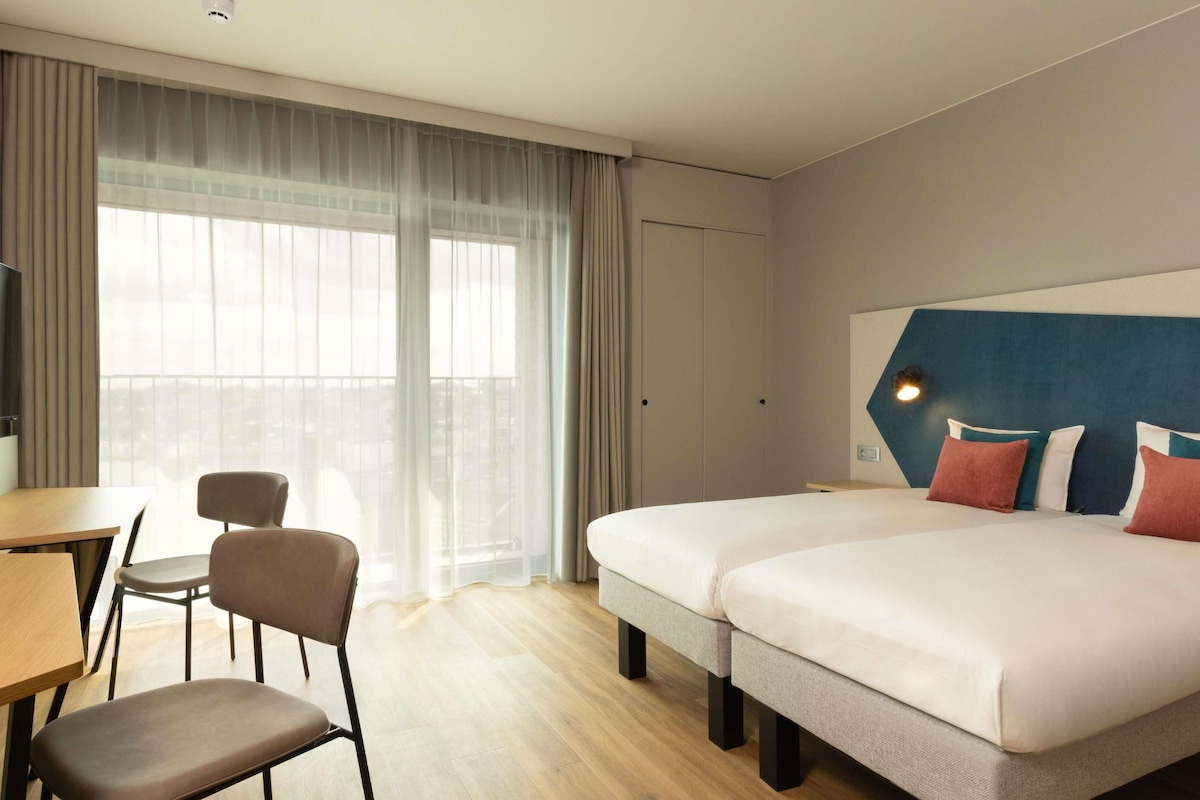 A hotel room with two beds, a desk, and a chair.