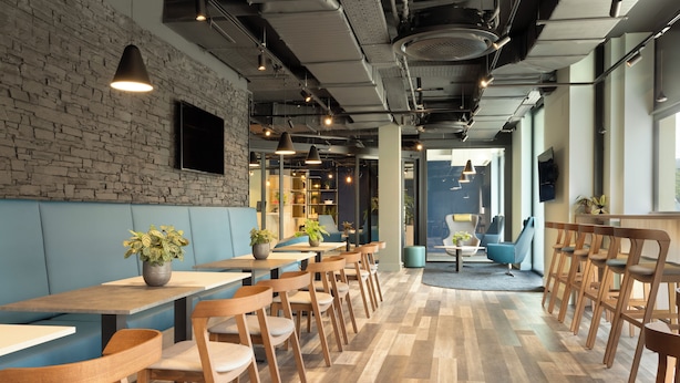 A modern restaurant with wooden tables and chairs, a brick wall, and large windows. - Adagio Antwerp City Center (Antwerp)