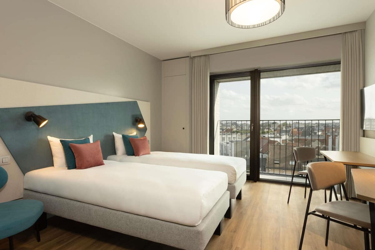 A hotel room with two beds, a dining area, and a balcony with a city view.