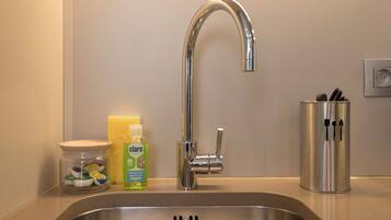 A stainless steel kitchen sink with a modern faucet, a jar of utensils, a bottle of dish soap, and a container with utensils.