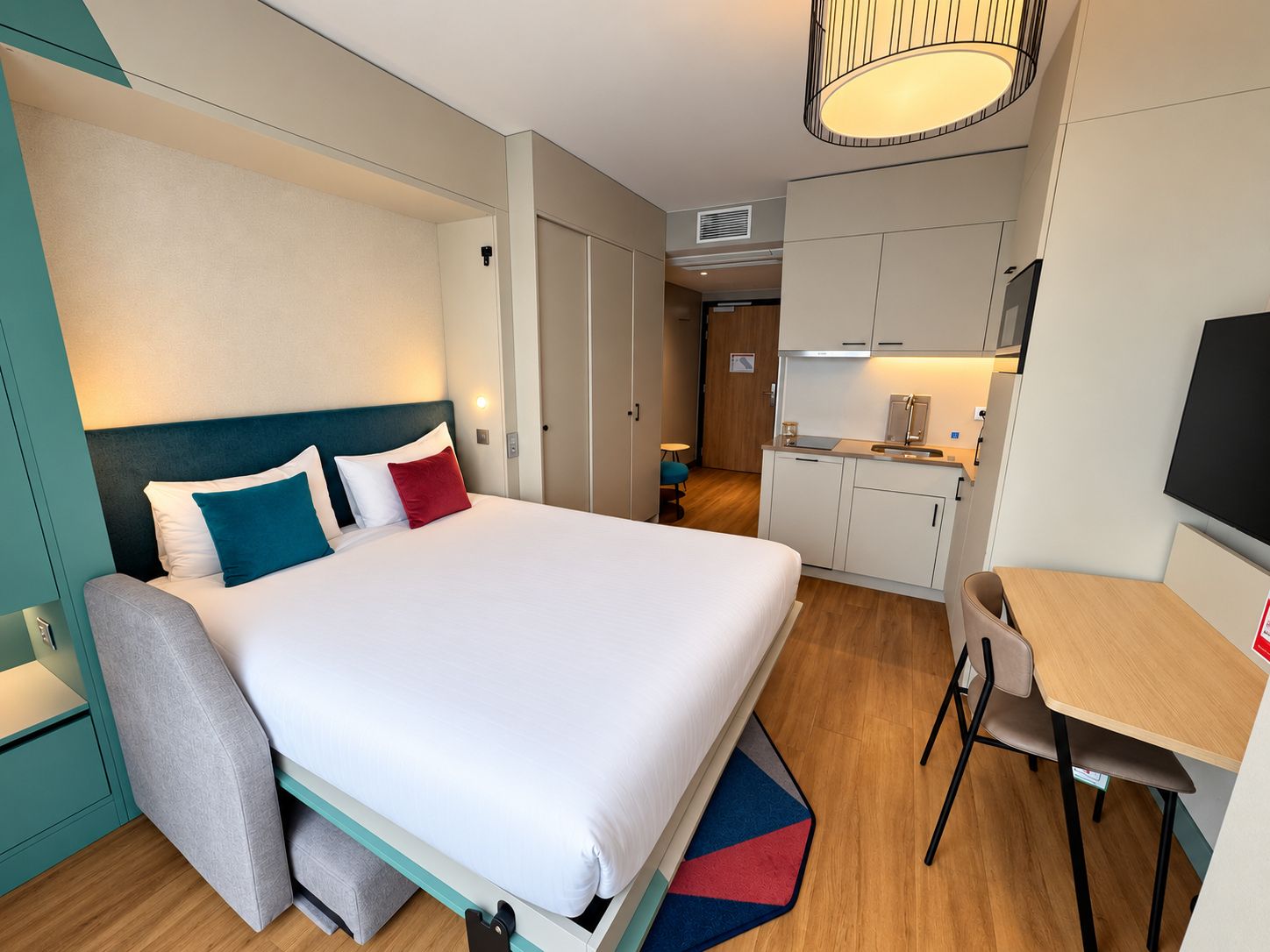 Una camera d'albergo con un letto, una scrivania, una sedia, angolo cottura e televisore.