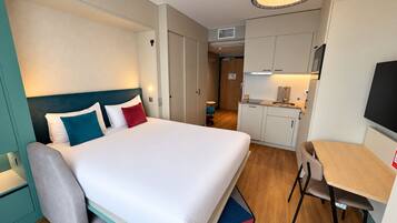 Una camera d'albergo con un letto, una scrivania, una sedia, angolo cottura e televisore.