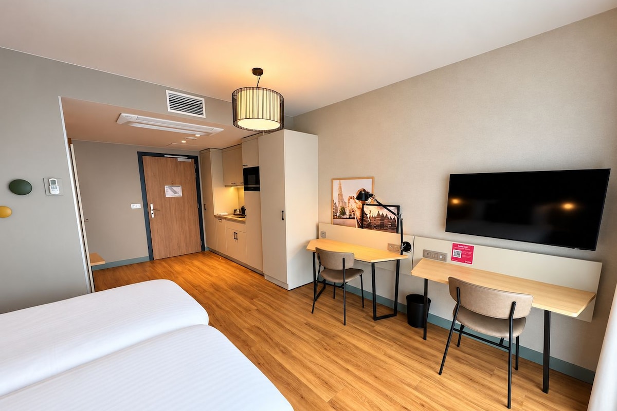 A hotel room with a bed, a desk with a chair, a television, and a picture on the wall.