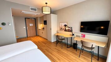 Une chambre d’hôtel avec un lit, un bureau et une chaise, une télévision et un tableau au mur.