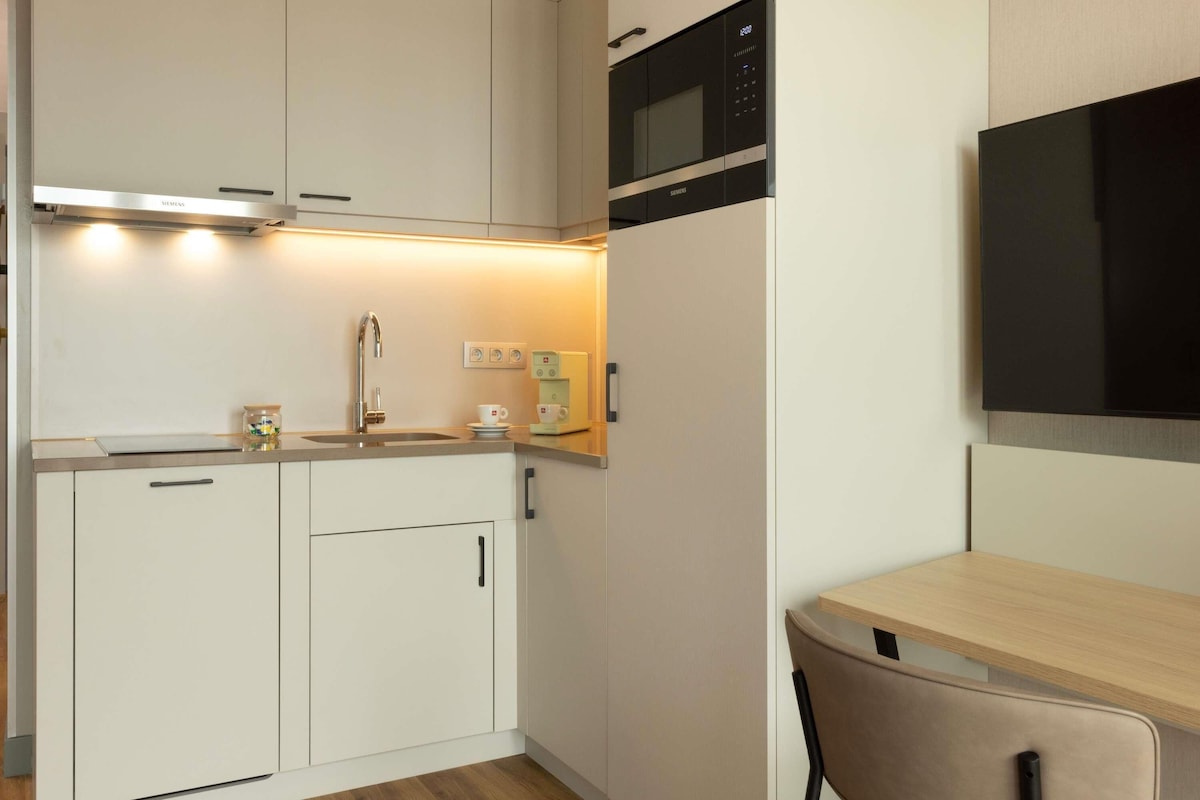 A compact kitchen with white cabinets, a microwave, a coffee machine, and a small table.