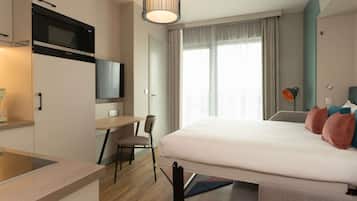 A modern hotel room with a bed, a desk, a chair, a television, and a window with curtains.