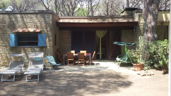 A stone building with a patio area featuring a table and chairs, a swing chair, and a potted plant. - Casa Alvino, Castiglione della Pescaia, Roccamare, private beach (Castiglione della Pescaia)
