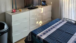 A bedroom with a bed, a TV on a white dresser, two wall-mounted lamps, and a window with curtains. - charming apartment - view of the Cavalaire bay (La Croix-Valmer)
