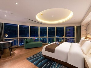A modern hotel room with a large bed, a desk, a green sofa, and a view of the city at night.