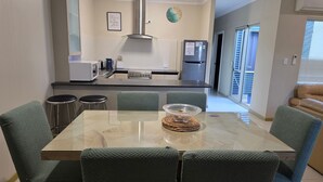 Ett modernt kök med ett matbord i glas, grönt klädda stolar, rostfria köksmaskiner och utsikt mot omgivningen.
