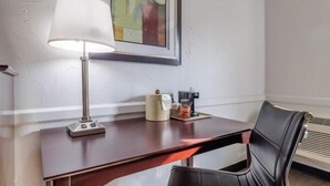 A hotel room with a desk, a chair, a lamp, a framed picture on the wall, and a radiator. - Motel 6 Dallas TX Downtown (DALLAS)