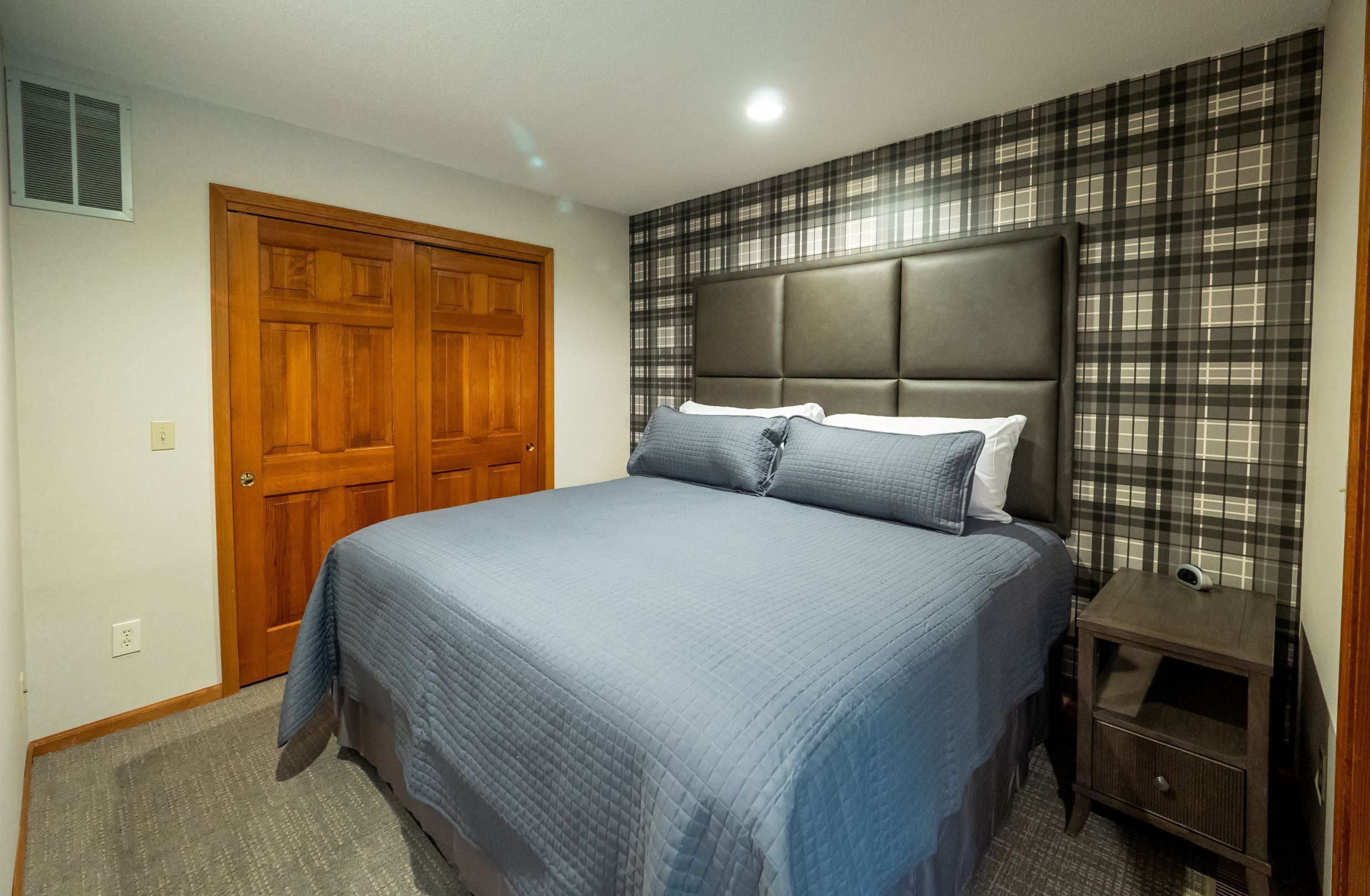 Un dormitorio con una cama grande, una puerta de madera y una mesita de noche con una lámpara.