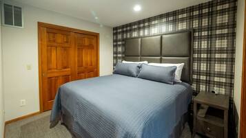 Un dormitorio con una cama grande, una puerta de madera y una mesita de noche con una lámpara.