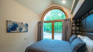 Quarto com cama grande, janela com cortinas, quadro na parede e vista para árvores lá fora.