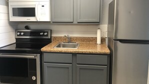 Una cocina con gabinetes grises, un refrigerador de acero inoxidable, un microondas, una estufa y un lavamanos.