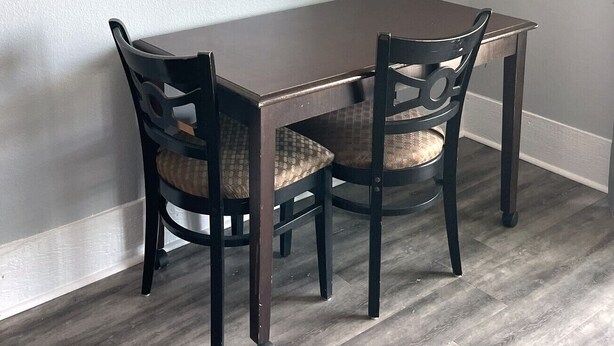 Un comedor con una mesa y dos sillas, un cuadro enmarcado en la pared y una pared de color claro.