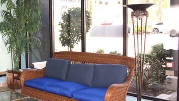A wicker sofa with blue cushions, a glass coffee table, and a tall floor lamp.