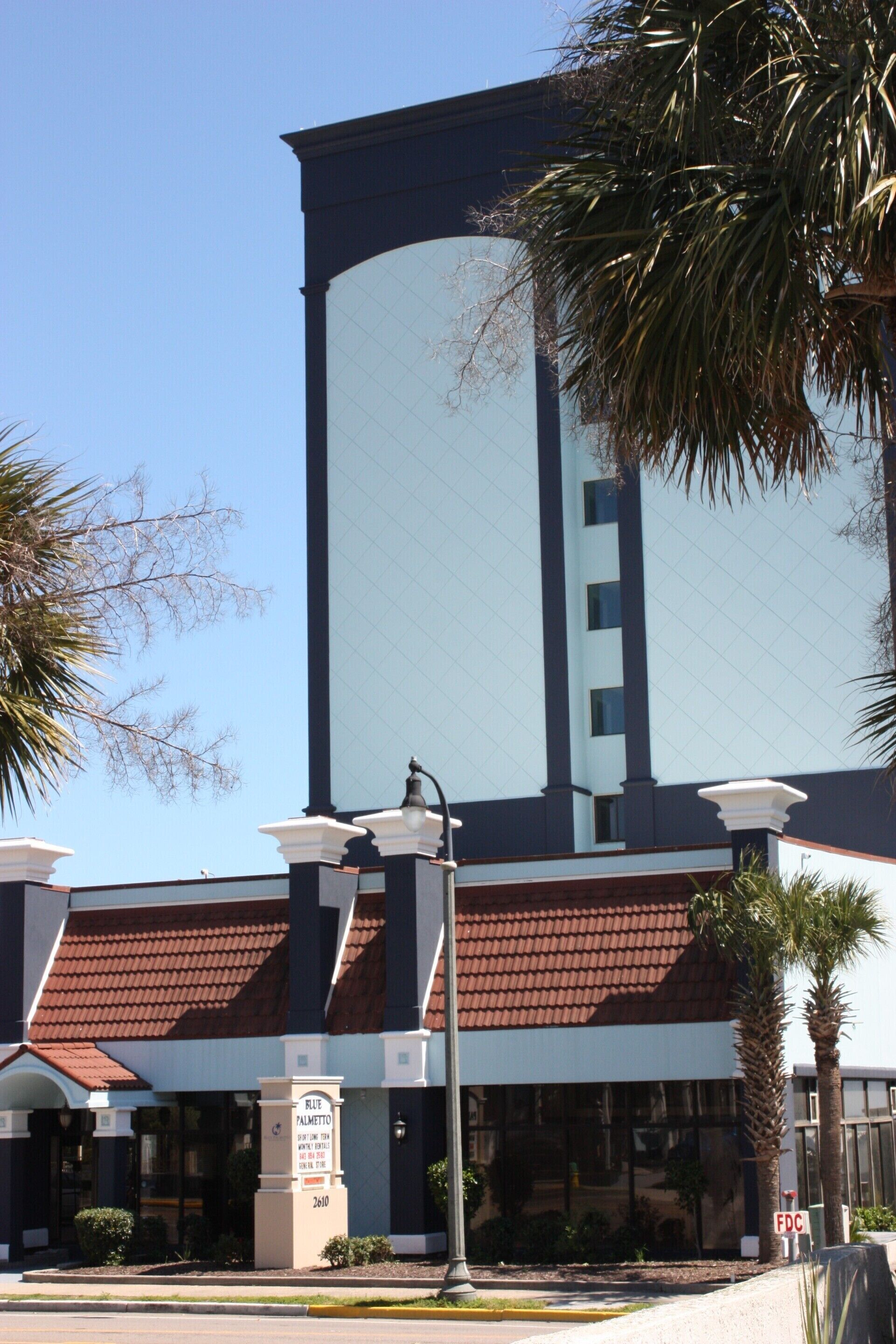A building with a large vertical sign, a red-tiled roof, and a signpost with a name plaque.