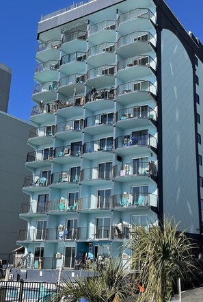 A multi-story hotel with balconies, a pool area, and a clear sky.