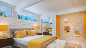 Een moderne slaapkamer met een groot bed, nachtkastjes, een hangstoel en een klein tafeltje met een lamp.