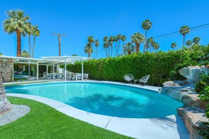 A swimming pool with a patio area, surrounded by palm trees and a stone wall. - Midcentury Masterpiece in Deepwell Estates - Pool and View  (Palm Springs)