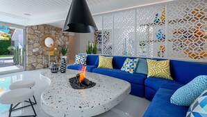 Een moderne woonkamer met een blauwe bank, een ronde stenen tafel met een haardvuur, en een wit plafond.