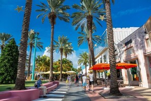 A pedestrian walkway lined with palm trees and outdoor seating areas with umbrellas.