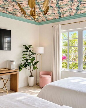 A hotel room with a bed, a desk with a coffee maker, a potted plant, a pink chair, and a large window with a view of greenery. - Villa Antonio | Art Deco Stay on Ocean Drive (Miami Beach)