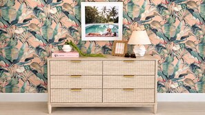A room with a patterned wallpaper, a framed photo, a lamp, and a wicker side table with books and a plant. - Villa Antonio | Art Deco Stay on Ocean Drive (Miami Beach)