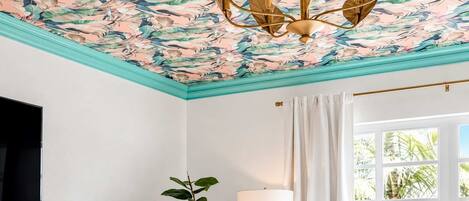 A room with a ceiling mural, a plant, a lamp, and a window with curtains.