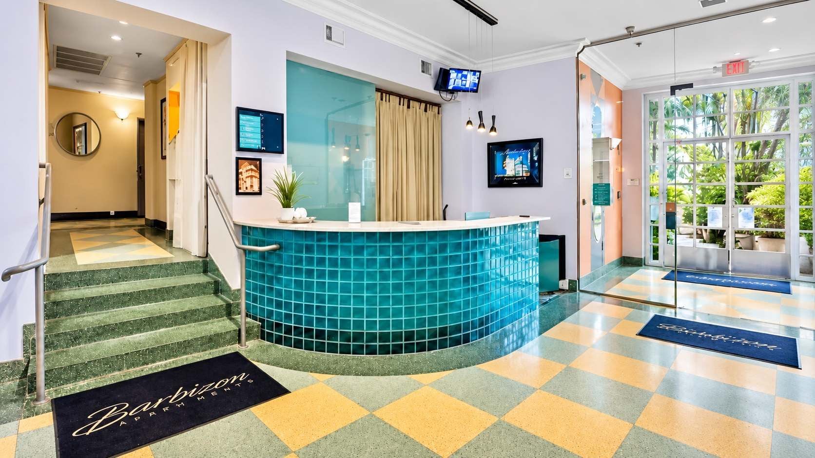 A hotel lobby with a reception desk, a staircase, and a large window with a view of greenery.