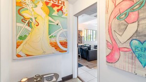 Een gang met twee grote kunstwerken, een moderne kantoorruimte en een klein tafeltje met een kaars en een klok.