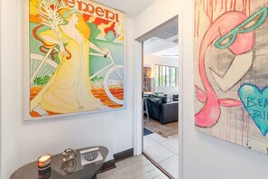 A hallway with two large artworks, a modern office space, and a small table with a candle and a clock. - Oceanfront Oasis: 2-BR Apartment on Ocean Drive (Miami Beach)