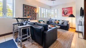 A modern living room with a sectional sofa, a coffee table, and a dining area with a table and chairs. There are large windows providing natural light and a ceiling fan. - Oceanfront Oasis: 2-BR Apartment on Ocean Drive (Miami Beach)