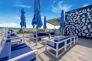 A rooftop lounge with blue cushioned seating, umbrellas, and a patterned wall.