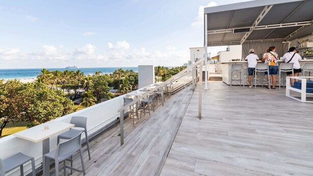 A rooftop bar with a view of the ocean, outdoor seating, and a bar area with staff. - Oceanfront Oasis: 2-BR Apartment on Ocean Drive (Miami Beach)