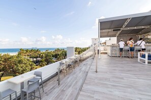 A rooftop bar with a view of the ocean, outdoor seating, and a bar area with staff. - Oceanfront Oasis: 2-BR Apartment on Ocean Drive (Miami Beach)